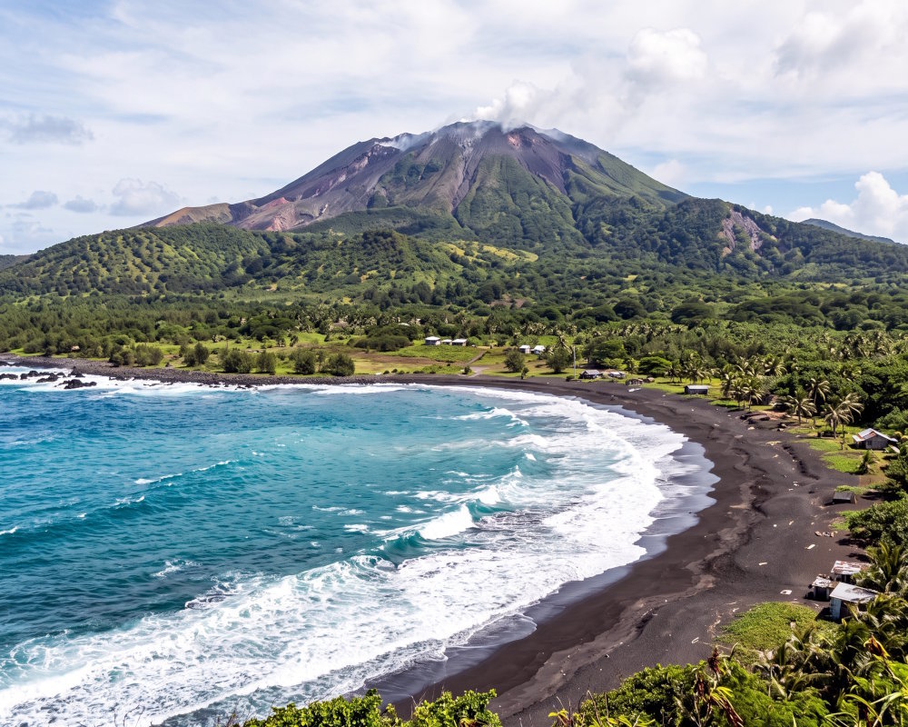 Black-sand beach with Pagan Volcano in the background on the wild coast of Pagan Island in the Northern Mariana Islands