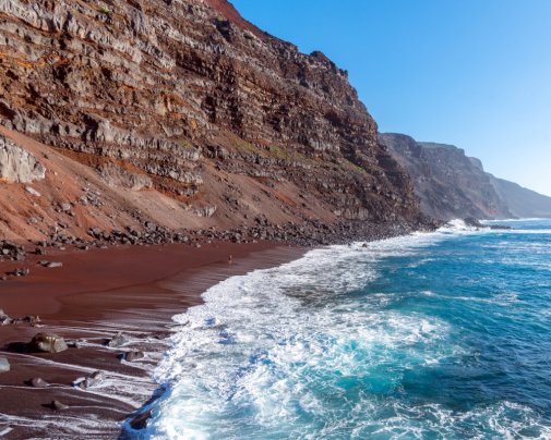 D'un sable rouge volcanique intense, la plage d'El Verodal offre un décor saisissant où falaises abruptes, reliefs basaltiques et vagues puissantes composent un paysage d'une beauté brute