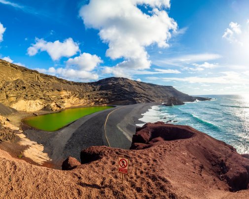 Entre les falaises rouges, le sable noir contraste avec l'océan bleu et la lagune verte, créant le spectacle unique d'El Golfo