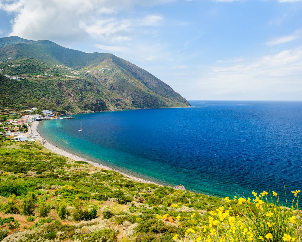 Une vue panoramique de la plage de galet del Porto avec au fond la jetée du port de Filicudi