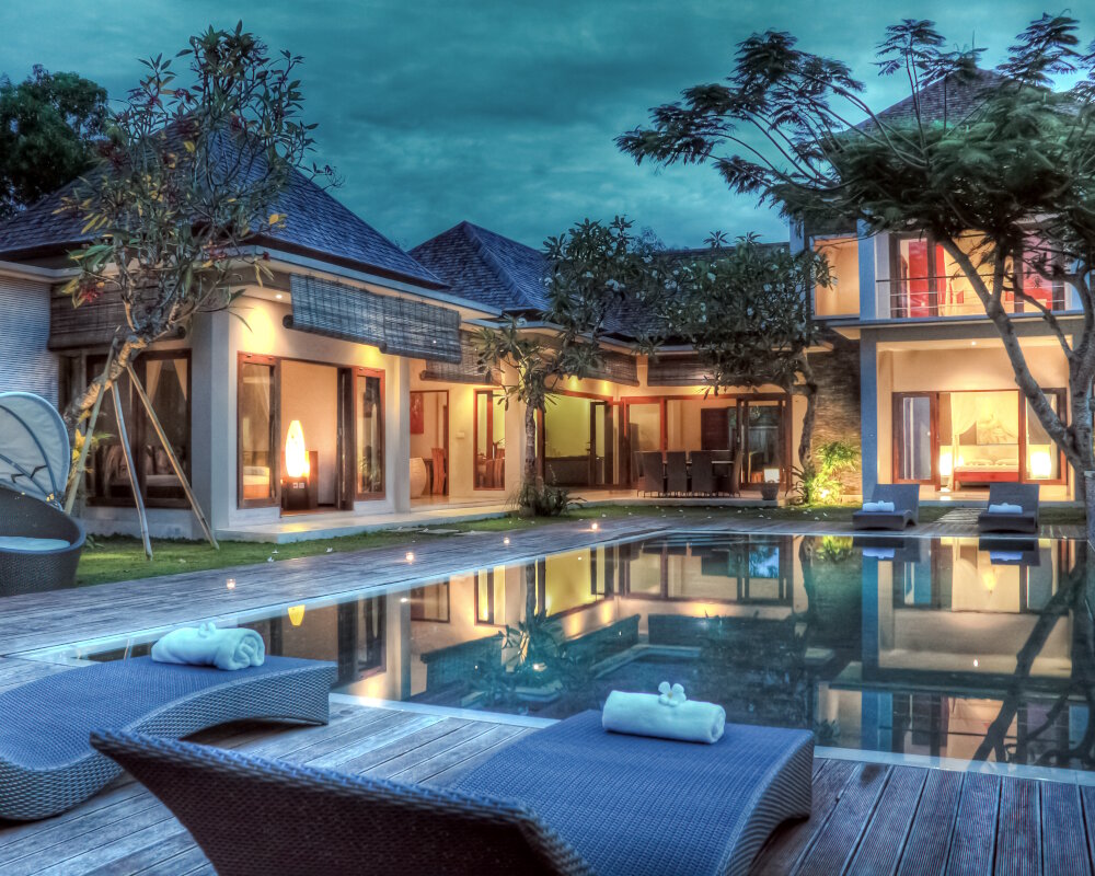 Les reflets nocturnes d'une villa tropicale se dessinent à la surface calme de sa piscine miroir