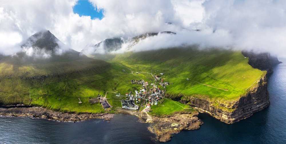 Aerial view of the village of Gjógv, located on Eysturoy island in the Faroe islands, surrounded by mountains and overlooking its famous natural gorge harbor